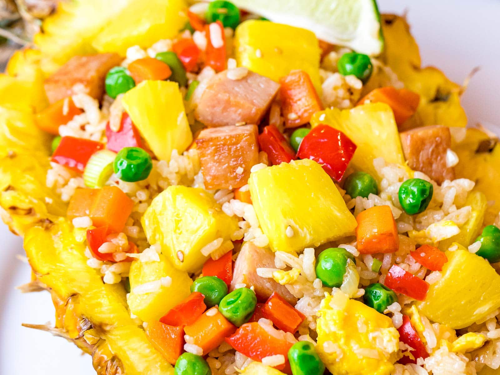 pineapple fried rice with pineapple chunks, ham, and peas served in a pineapple boat