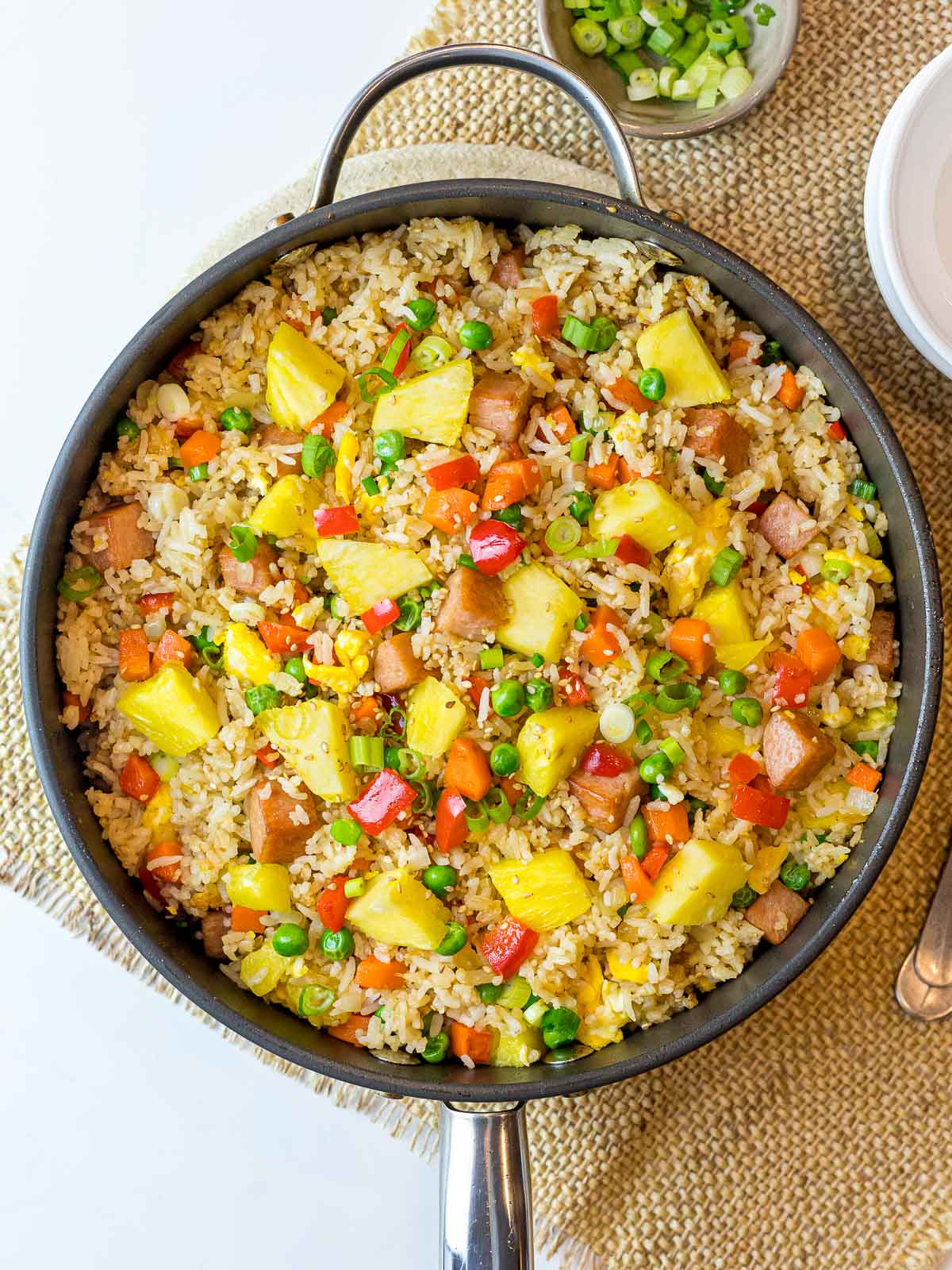 Thai pineapple fried rice with pineapples, red bell peppers, and scallions on a bamboo placemat