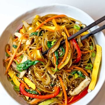 japchae noodles with red peppers, carrots, and shiitake mushrooms in a white bowl with chopsticks