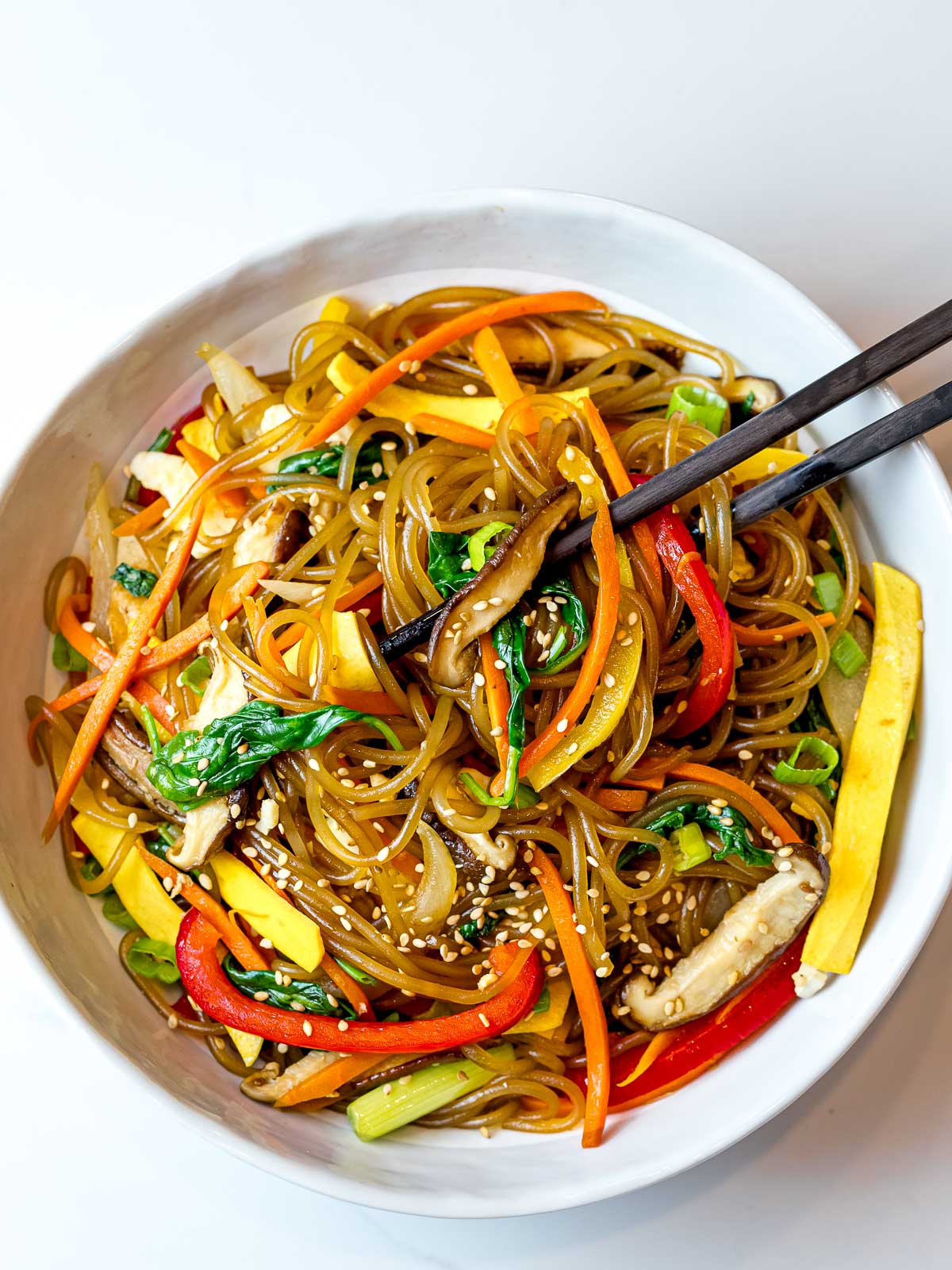 japchae noodles with red peppers, carrots, and shiitake mushrooms in a white bowl with chopsticks