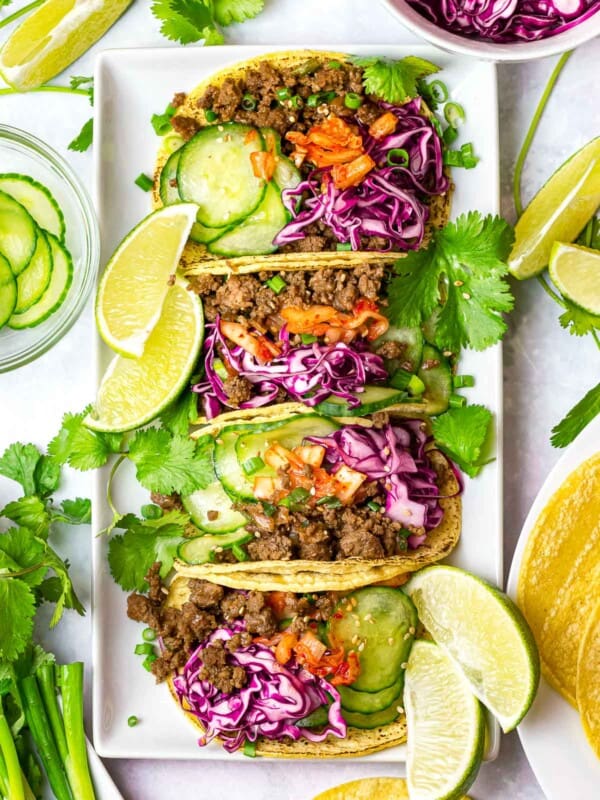 Korean beef tacos with purple slaw, kimchi, cucumbers, and lime on a white plate