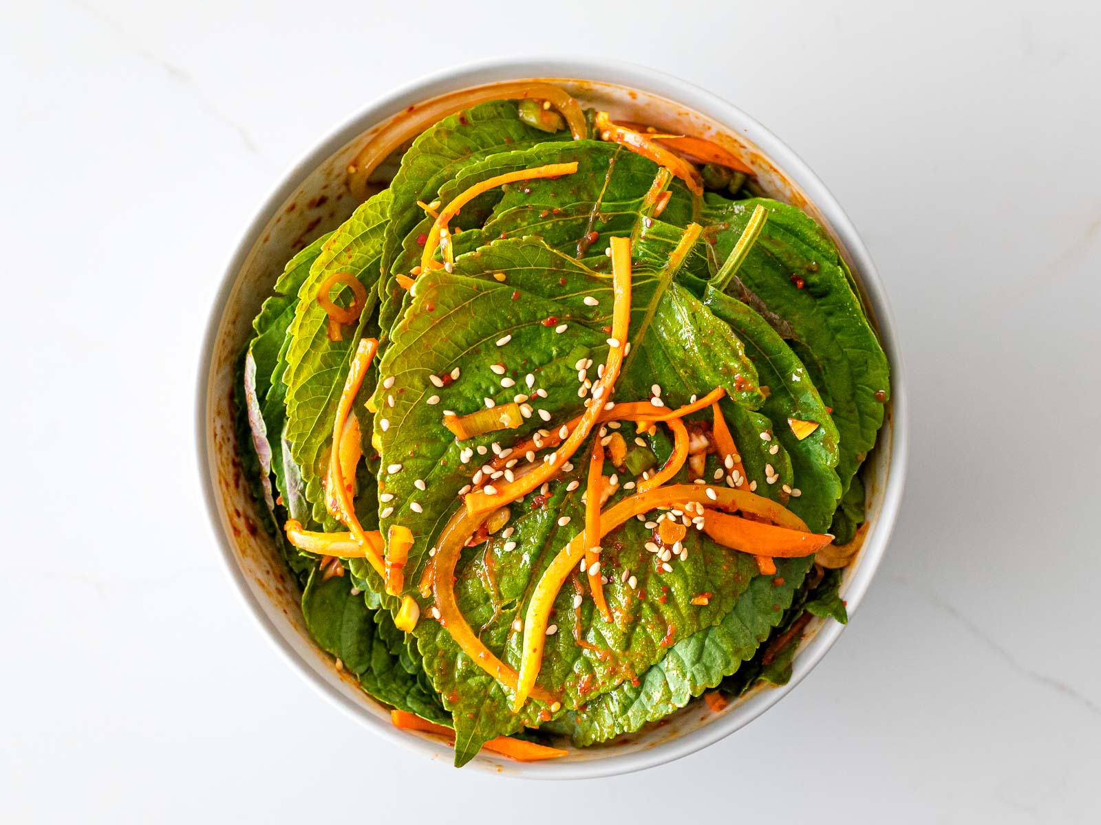 Korean perilla leaf kimchi in a white bowl with shredded carrots and sesame seeds