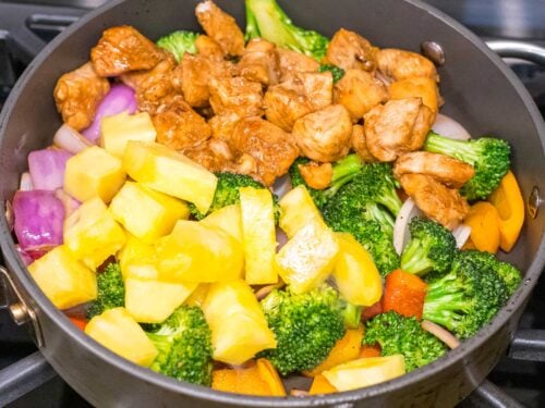 Hawaiian pineapple chunks, chicken, and veggies stir fried together in a pan