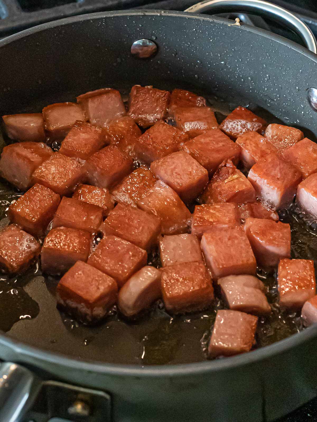 cubes of spam frying in a nonstick pan