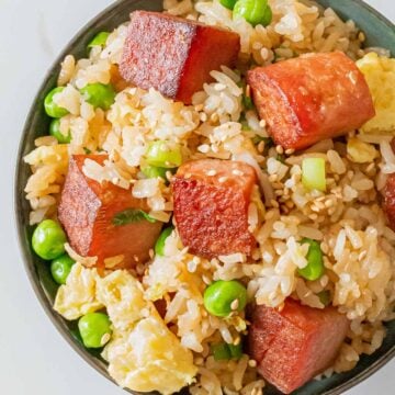 bowl of spam fried rice with crispy cubes of spam, eggs, green peas, and sesame seeds