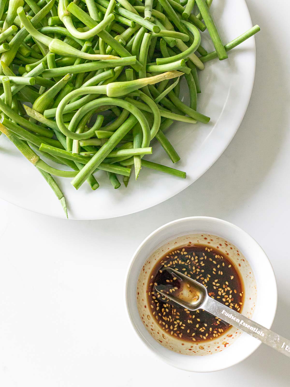garlic scapes on a white plate next to a bowl of sauce