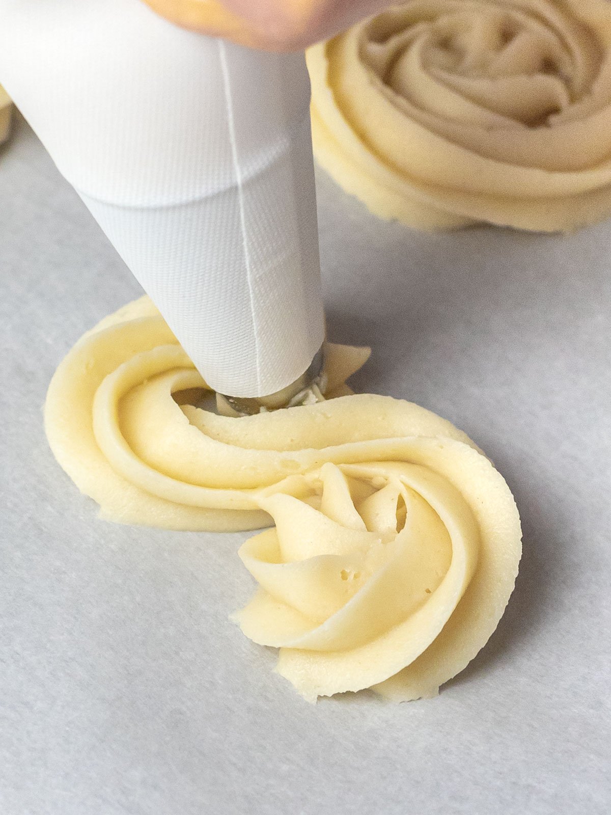 butter cookies being piped with a piping bag onto parchment paper