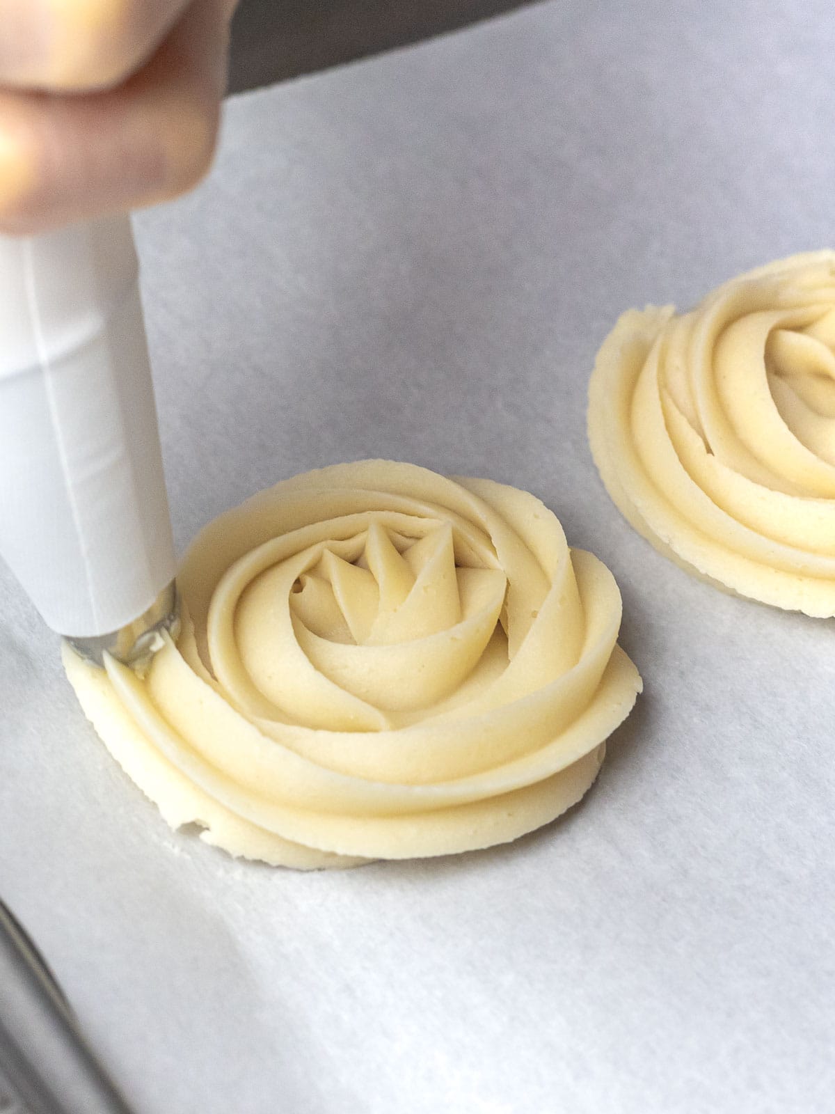 butter cookie dough being piped into rosettes with a piping bag