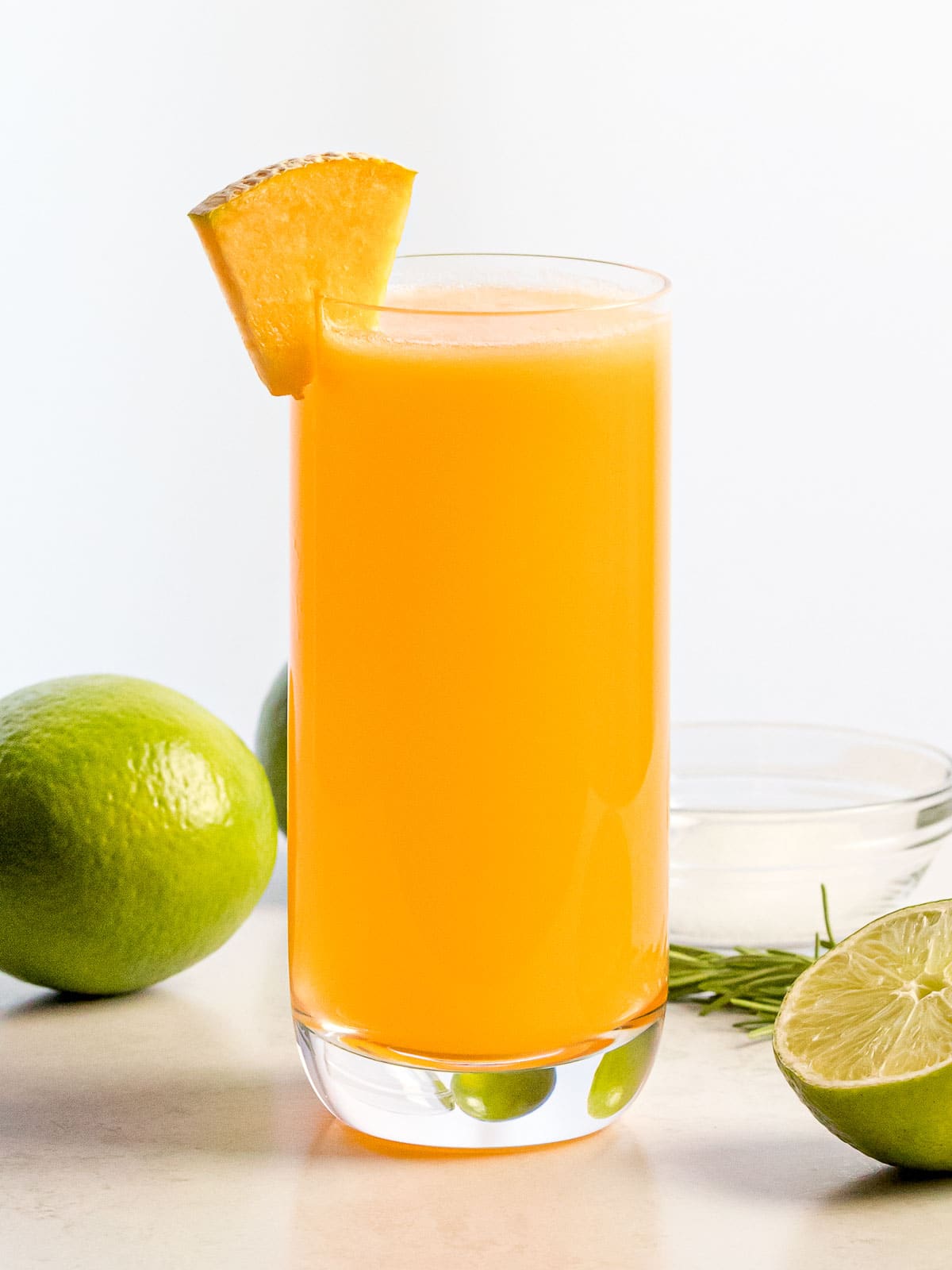 a glass of cantaloupe agua fresca next to limes