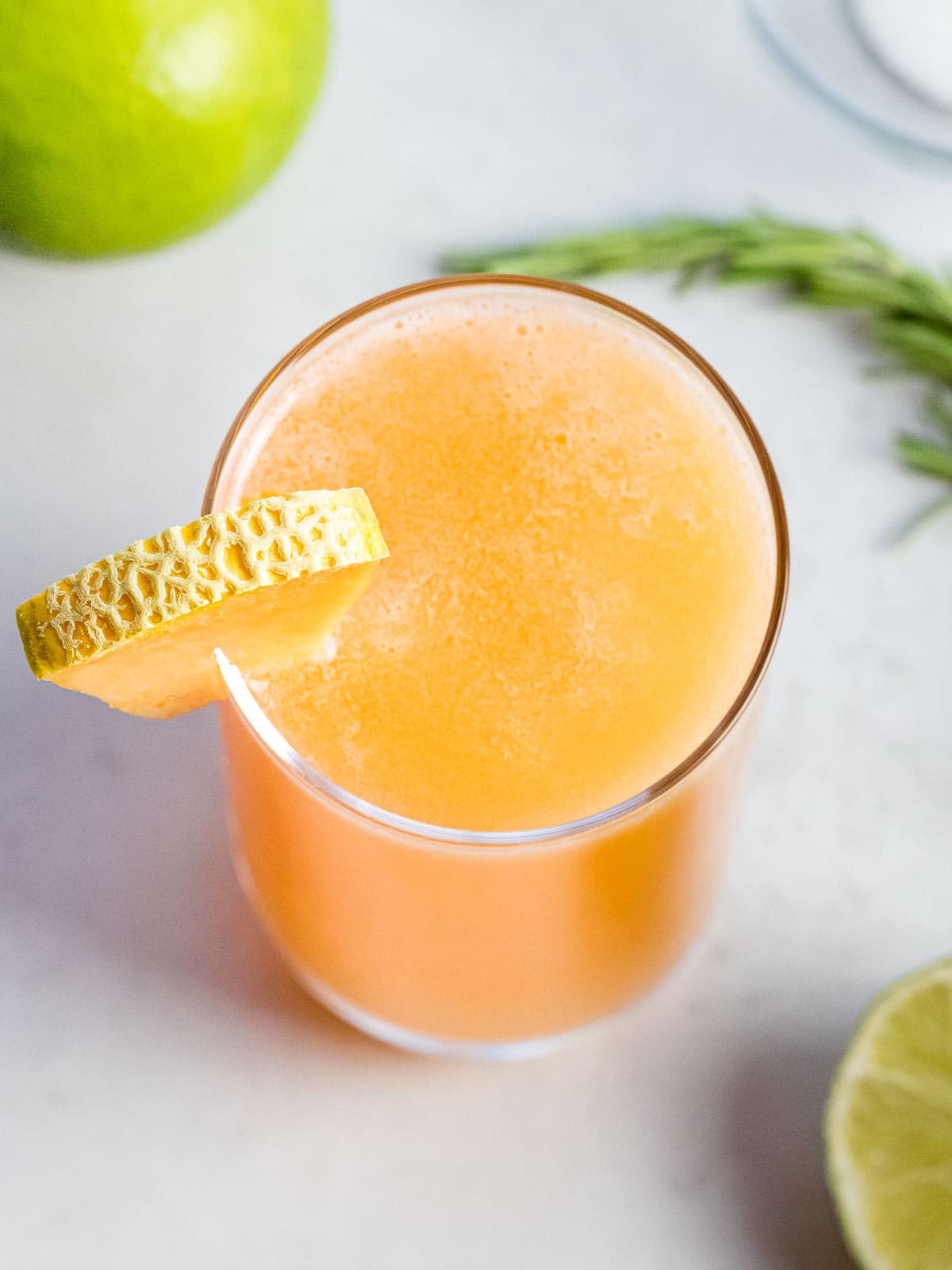glass of cantaloupe agua fresca next to lime and herbs
