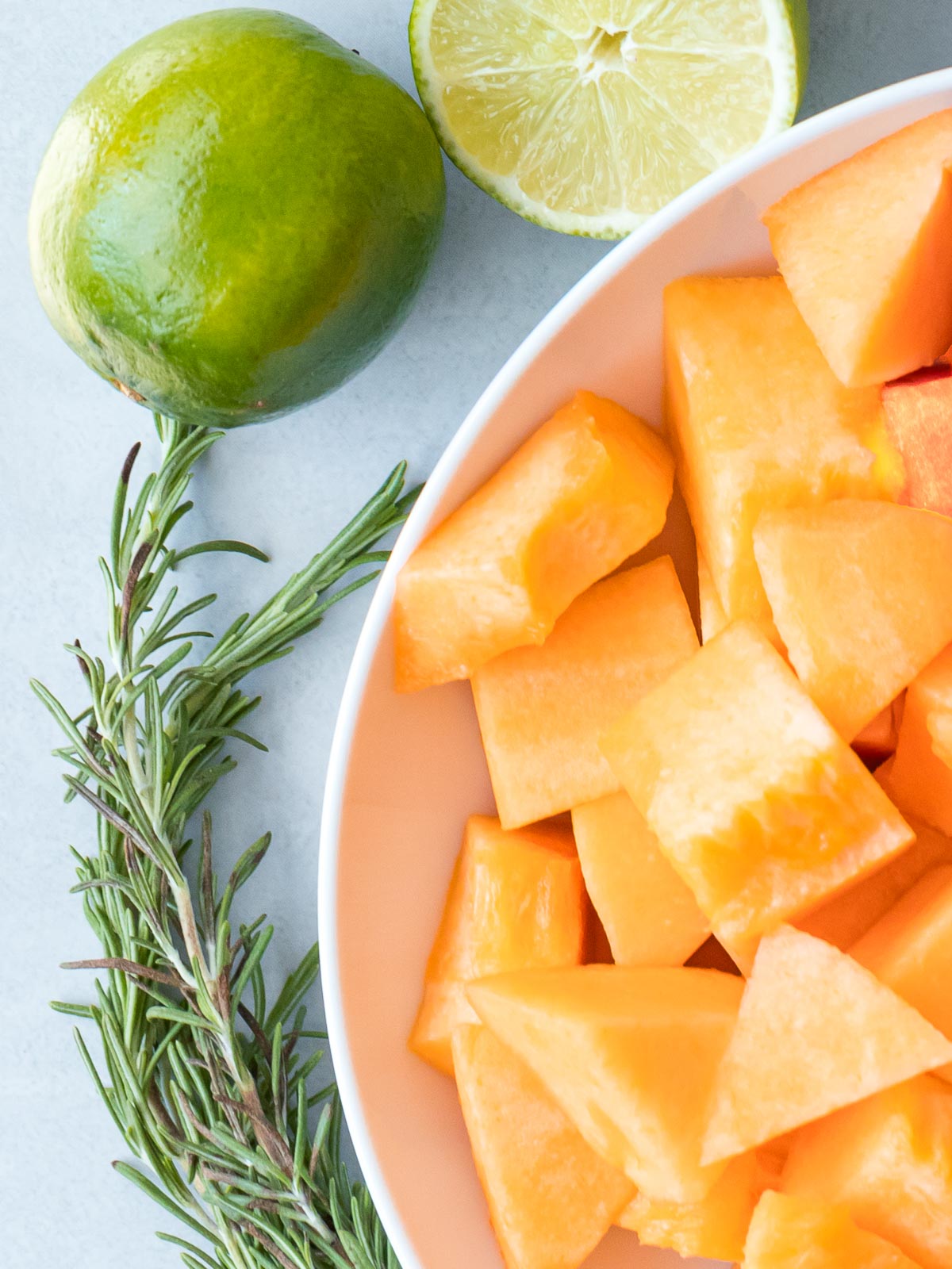 cantaloupe pieces in a bowl next to lime and herbs