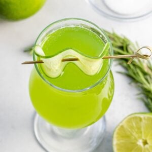 cucumber agua fresca with a slice of cucumber garnish next to lime and herbs