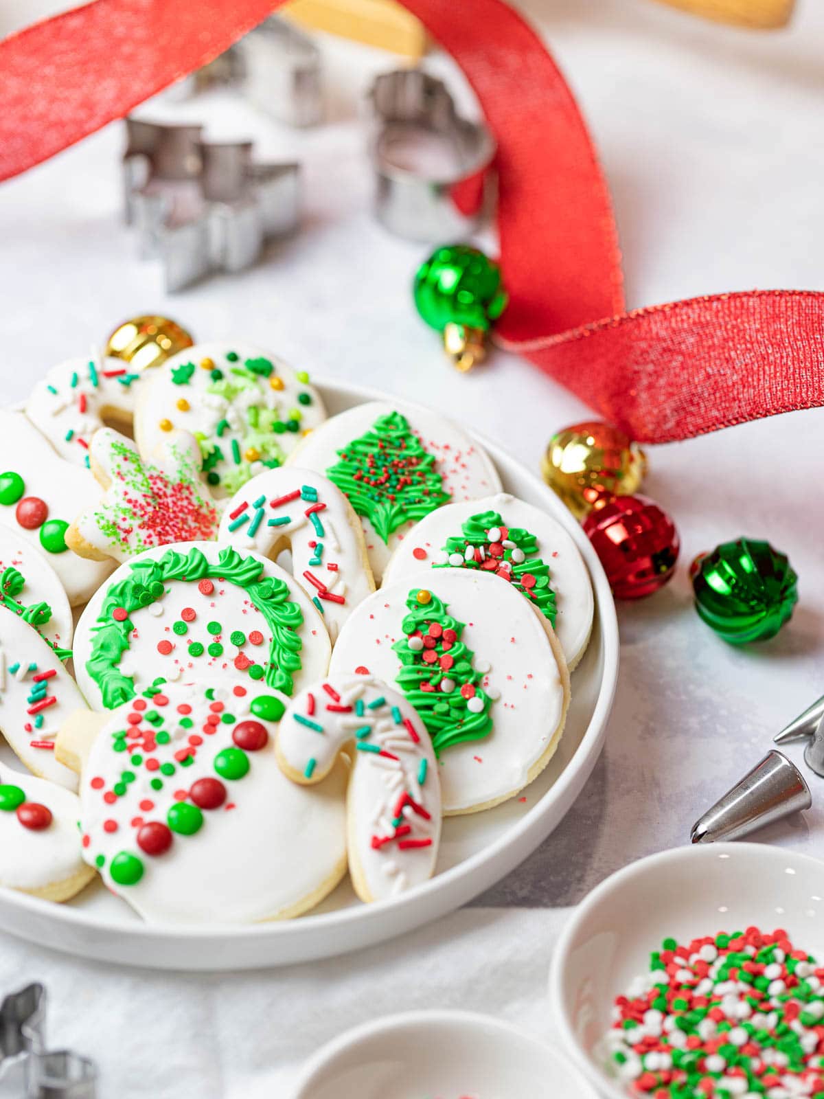 easy decorated Christmas cookies with icing and sprinkles next to ornaments, ribbon, and cookie cutters