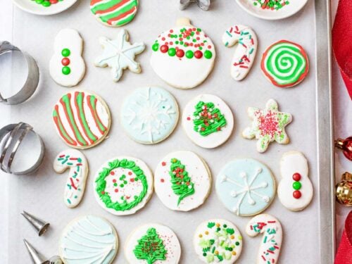 iced Christmas sugar cookies on a baking sheet next to ornaments, cookie cutters, and red ribbon