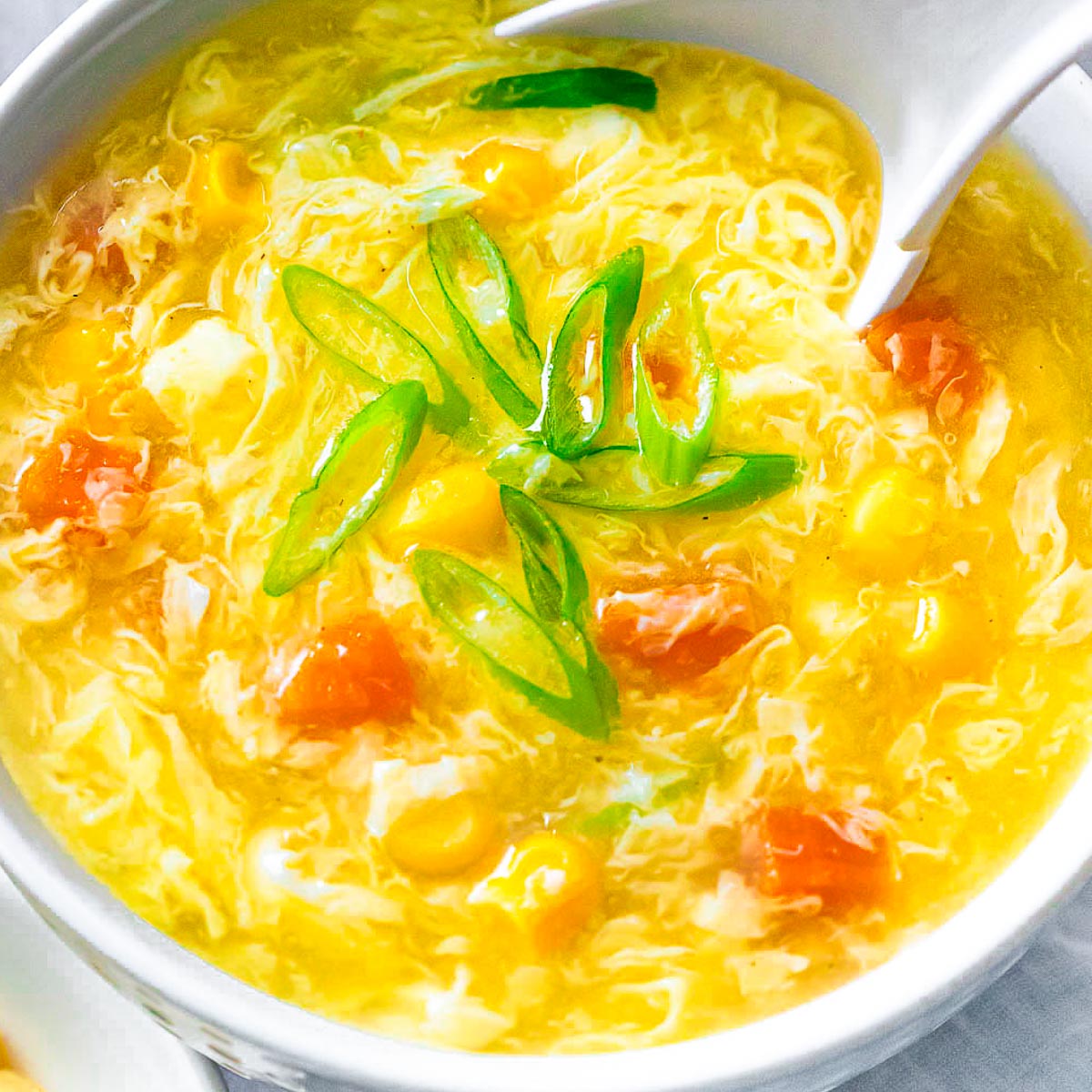 Bowl of restaurant style egg drop soup with corn, carrots, and egg flower ribbons with a soup spoon.