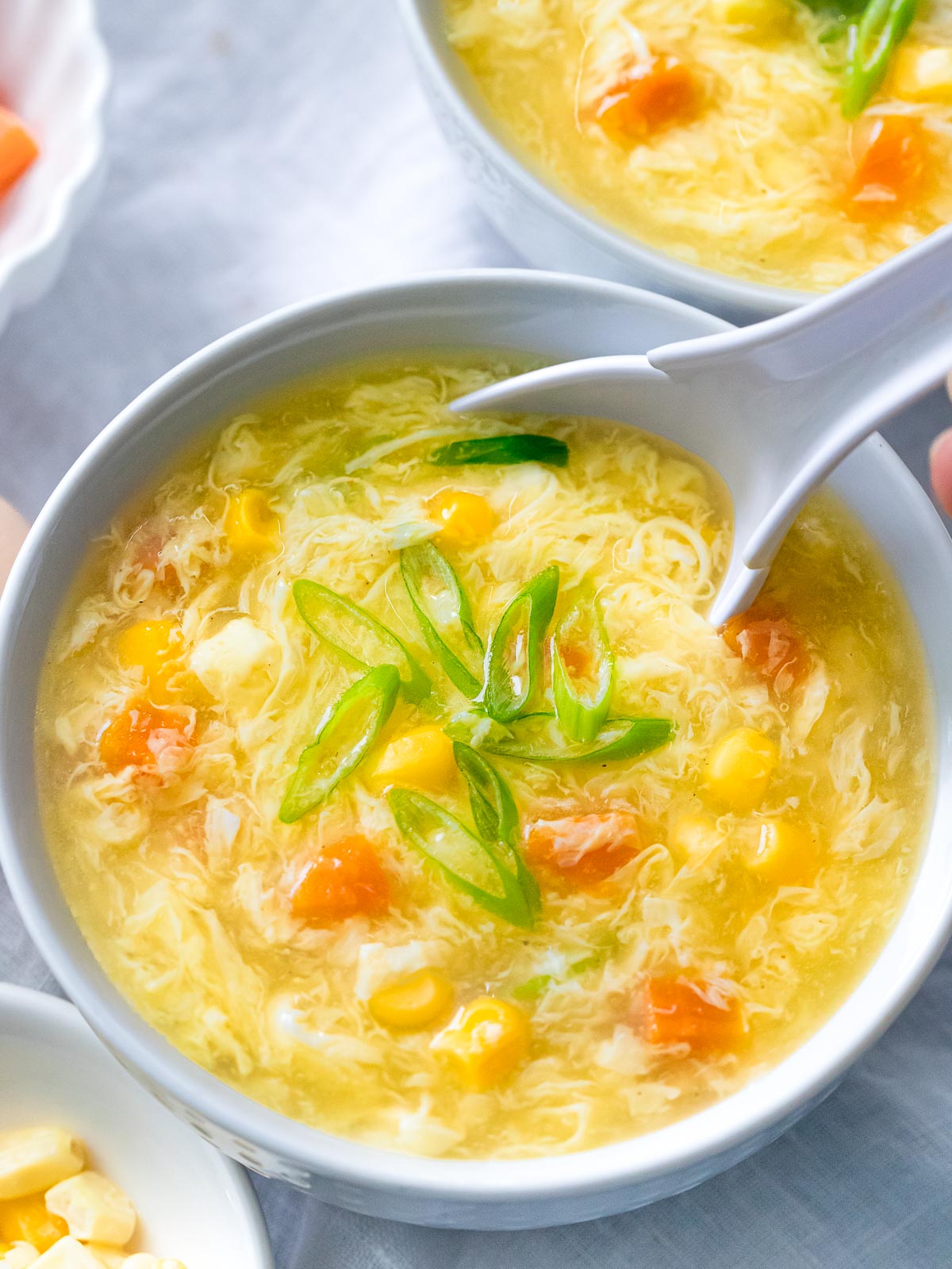 bowl of authentic egg drop soup with corn, carrots, and scallions with a spoon