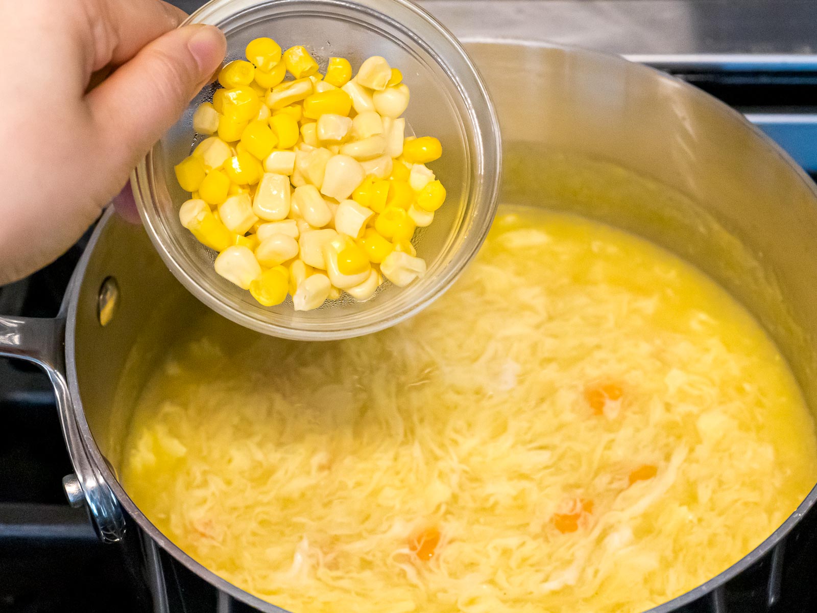 corn being added to egg drop soup in a pot