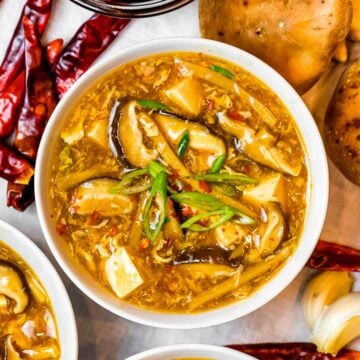 a bowl of Chinese hot and sour soup with mushrooms and tofu next to dried spicy chili peppers