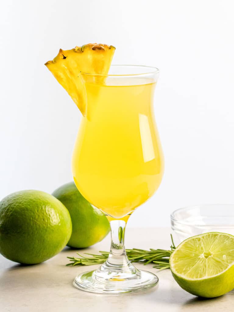 glass of pineapple agua fresca with a slice of pineapple next to limes