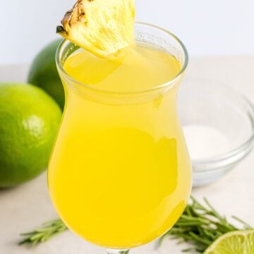 close up of pineapple agua fresca with a slice of pineapple next to lime