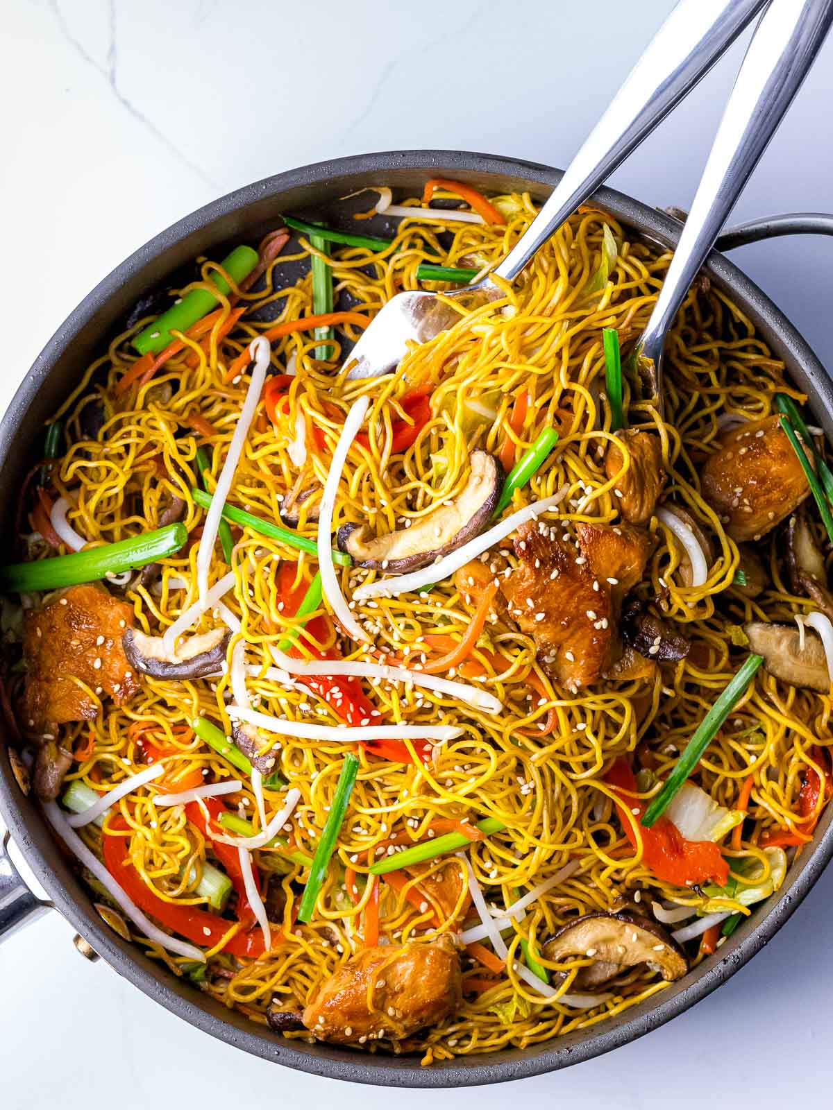 chicken chow mein noodles with vegetables and bean sprouts with serving utensils in the pan