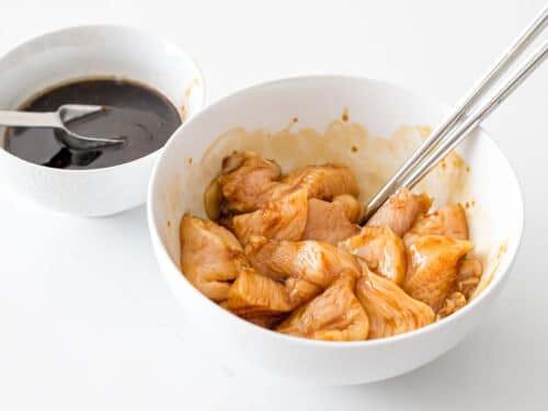 chicken breast mixed with soy marinade in a white bowl