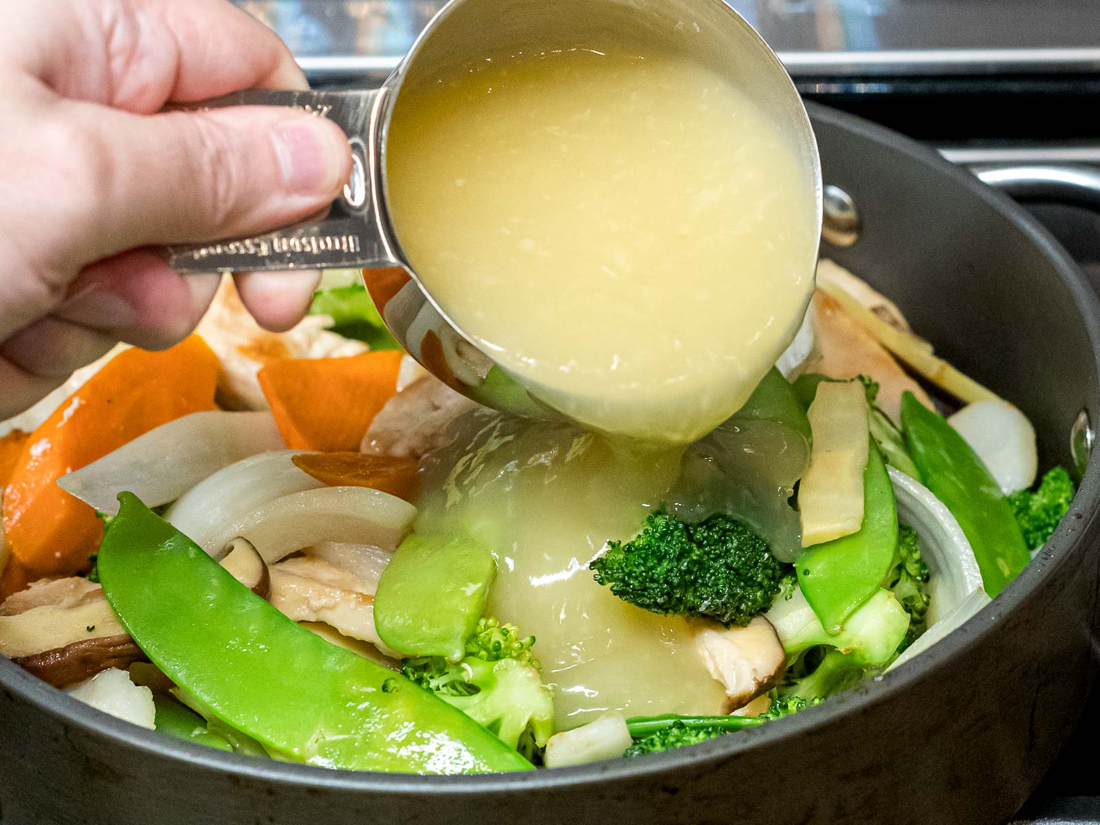 Moo goo gai pan sauce being added to chicken and vegetables stir fry