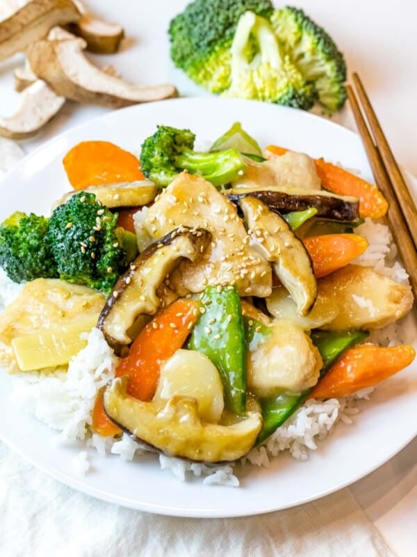 Chinese moo goo gai pan stir fry on a plate of rice next to chopsticks