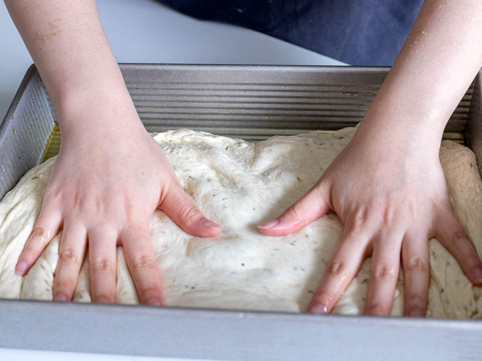 focaccia dough pressed into a baking dish with hands