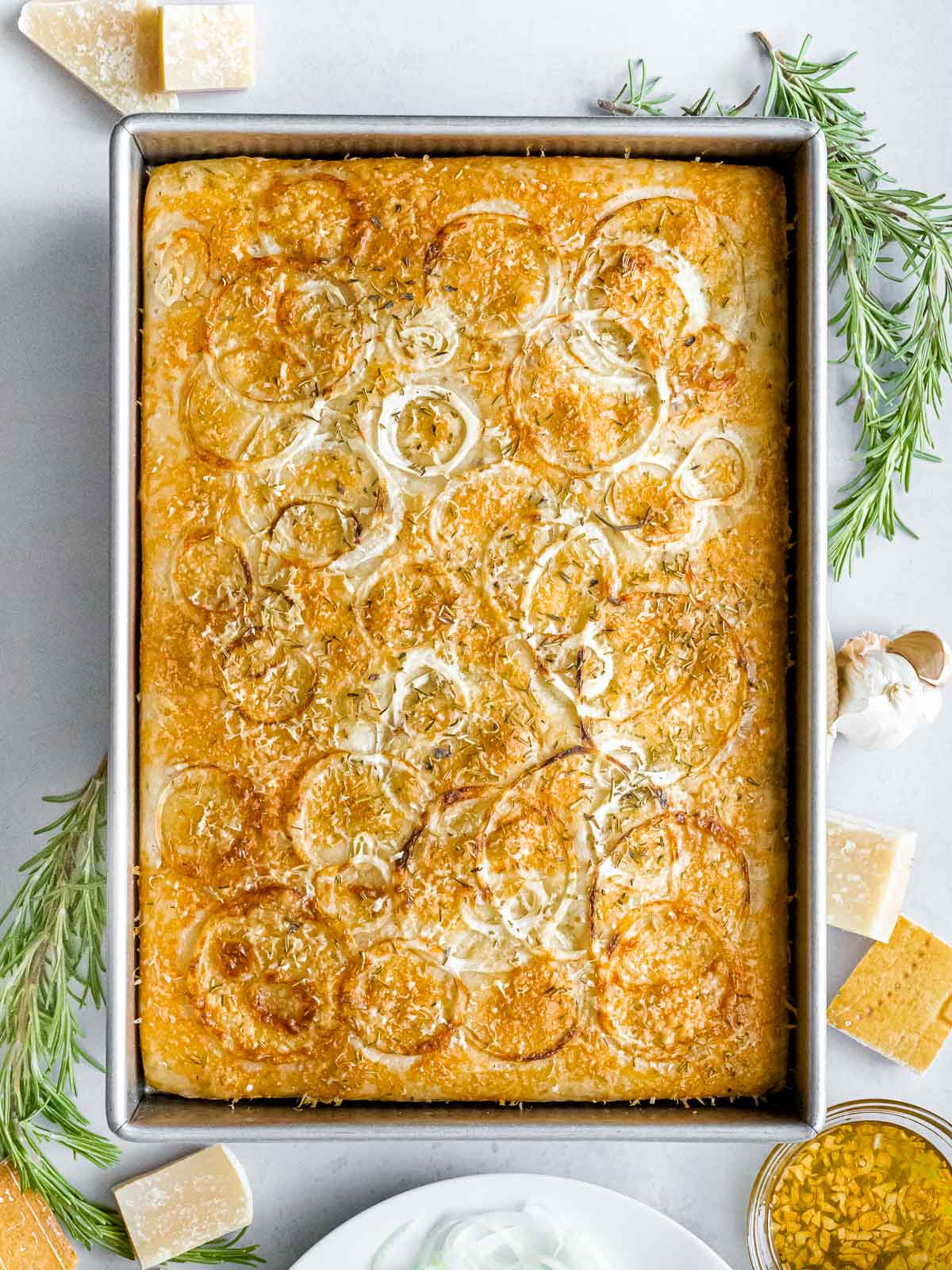 sourdough focaccia bread with rosemary, onions, and parmesan cheese in a baking pan