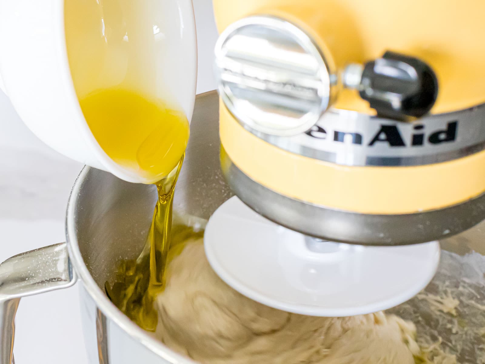 olive oil being added to focaccia dough being mixed in a stand mixer