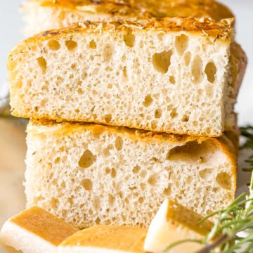 slices of sourdough focaccia bread stack on top of each other next to rosemary and parmesan