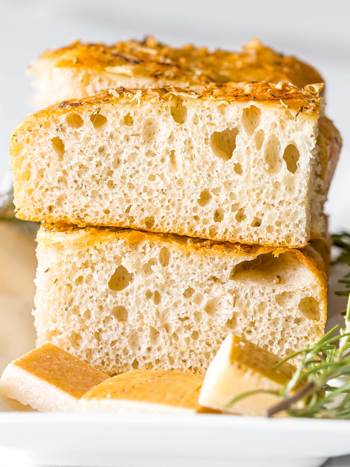 slices of sourdough focaccia bread stack on top of each other next to rosemary and parmesan
