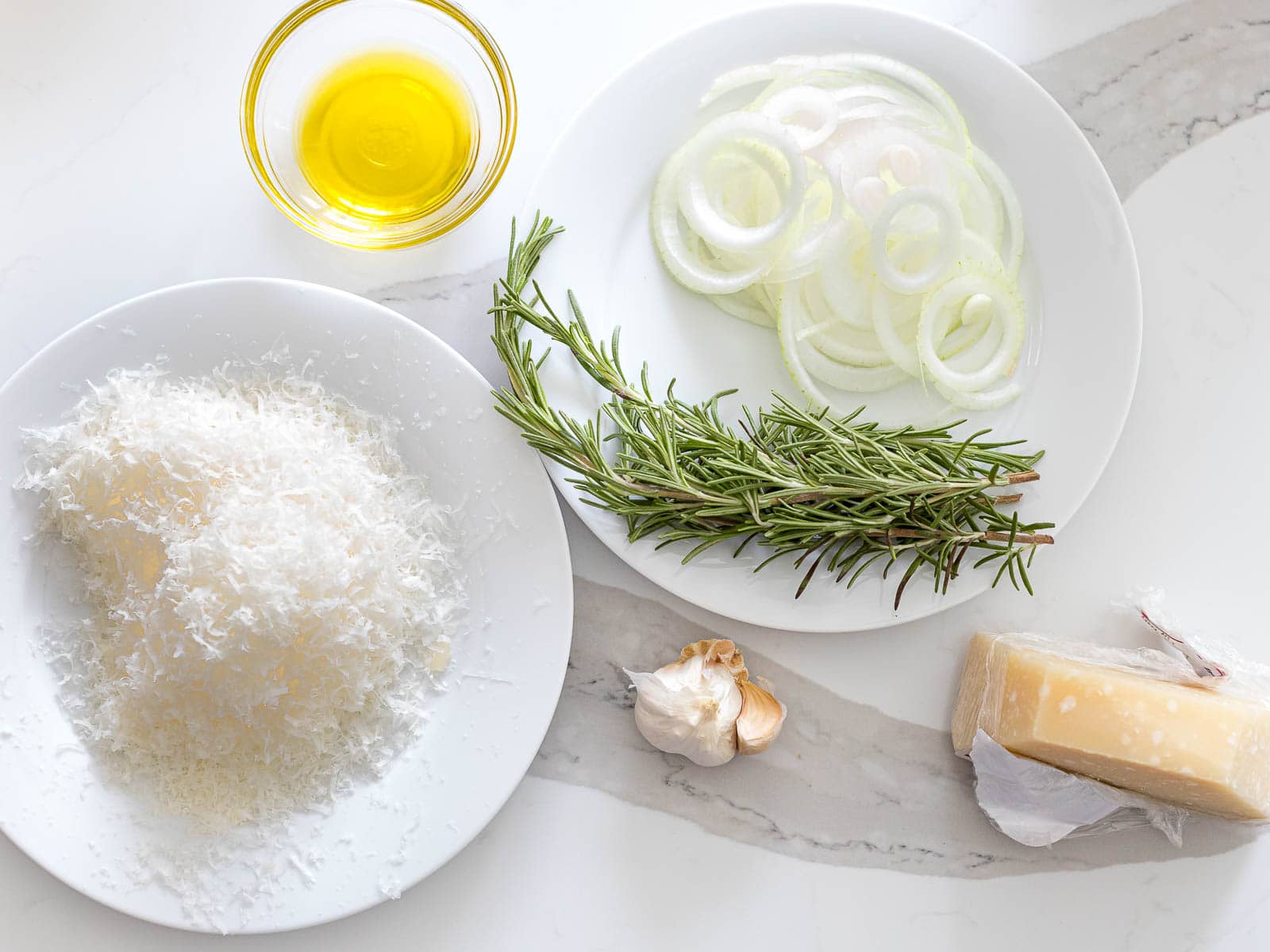 parmesan cheese, rosemary, sliced onions, and olive oil on a white counter
