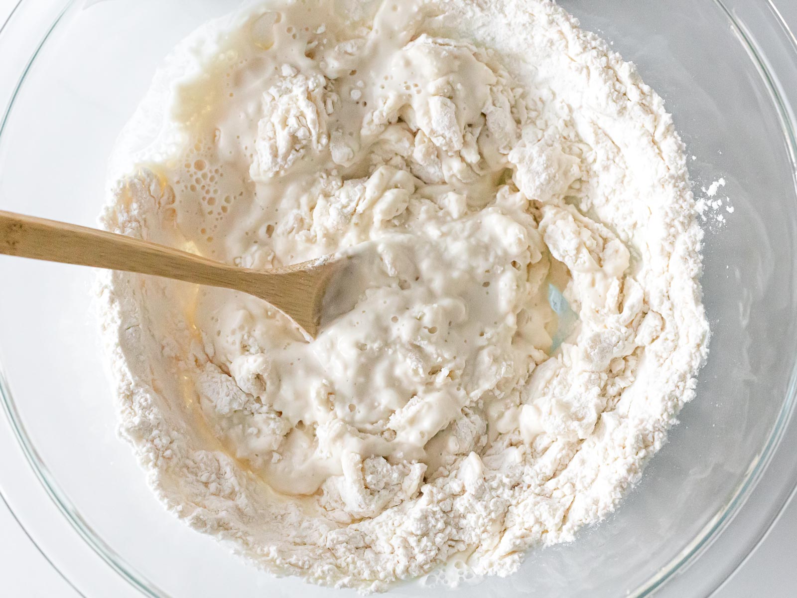 flour and water mixed in a glass bowl with a wooden spoon