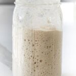 active sourdough starter in a glass mason jar showing bubbles and increase in volume