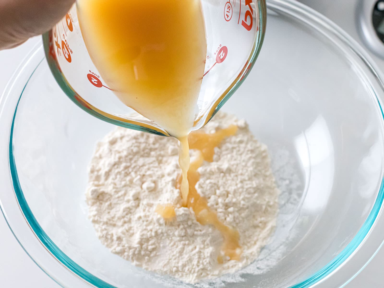 yeast water being poured into flour in a glass bowl
