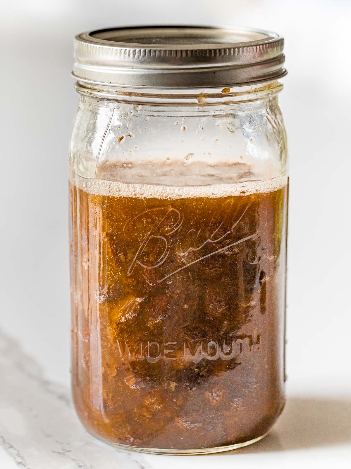 raisins fermenting in water with a foam layer on top inside a glass mason jar with a lid
