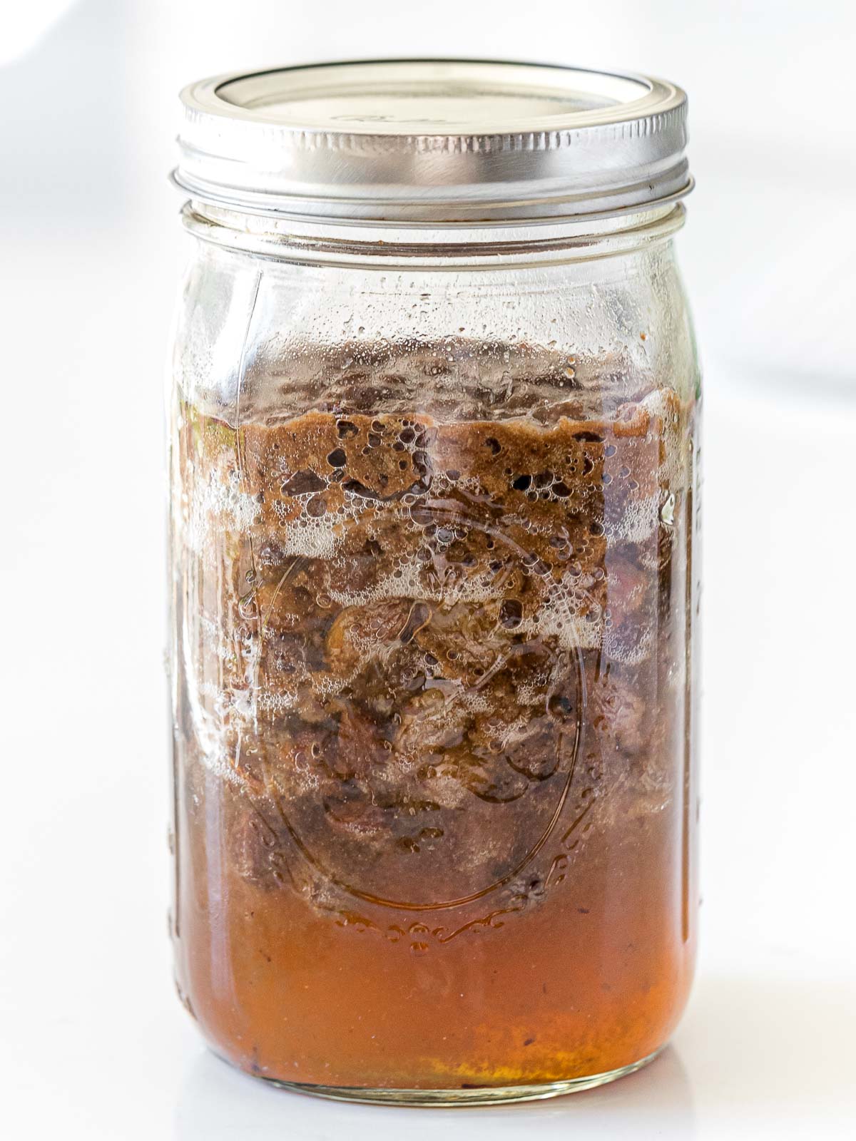 fermented raisin yeast water showing bubbles and floating raisins in a glass mason jar with a lid
