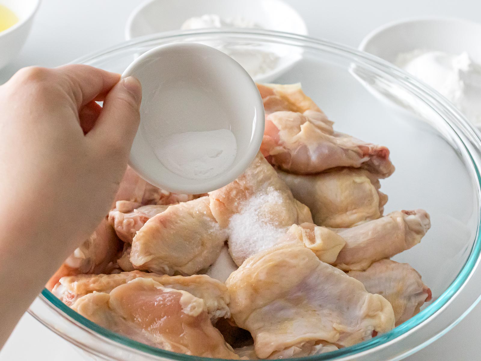 adding salt to raw chicken wings in a glass bowl