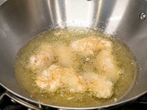 battered fried chicken wings in cooking oil in a metal pot