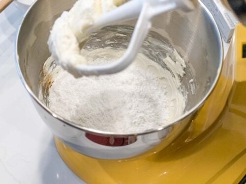 powdered sugar added to a mixing bowl with creamed butter and cream cheese