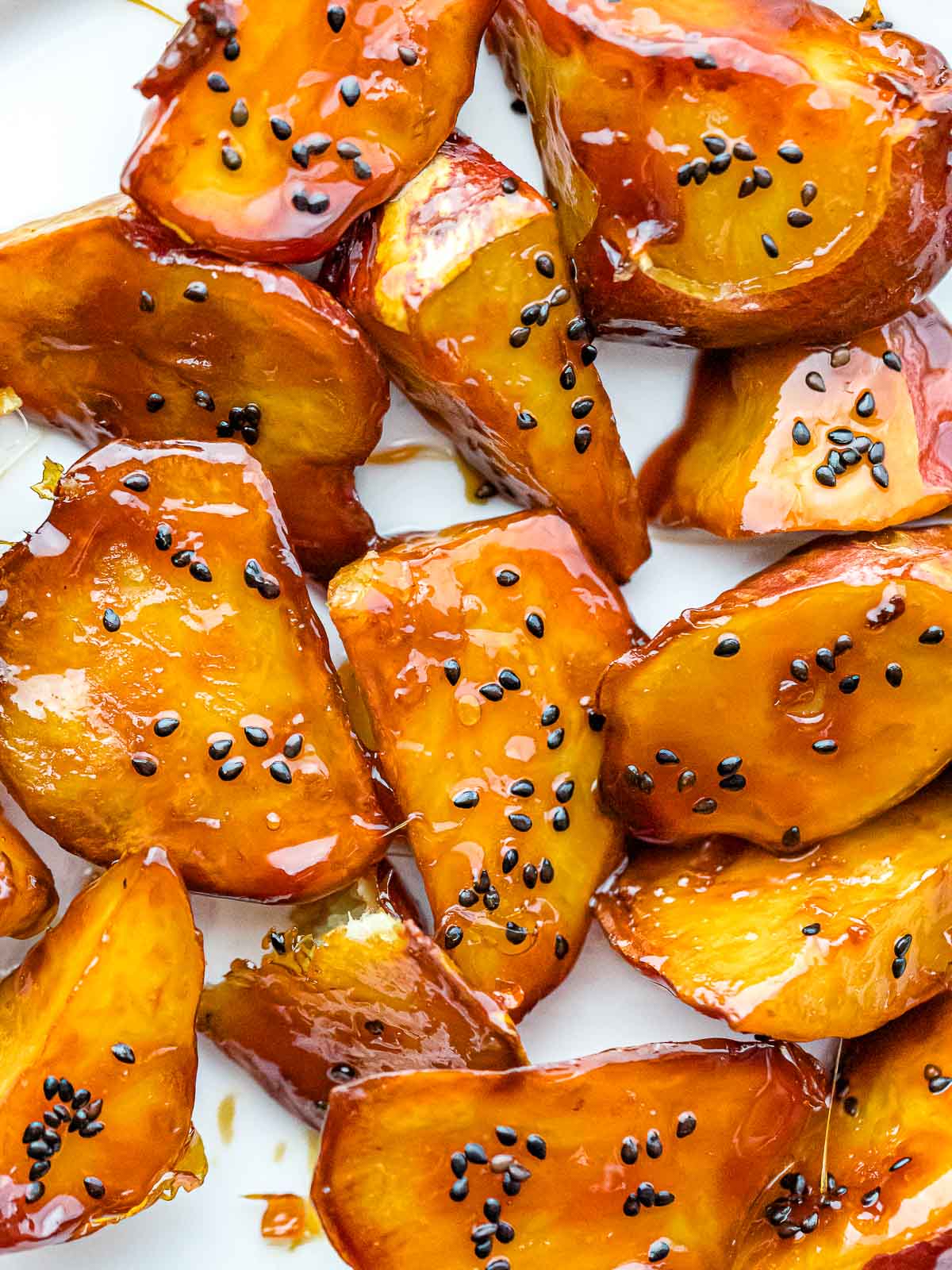 Korean candied sweet potatoes with golden caramel coating and black sesame seeds on a white plate