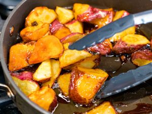 sweet potato pieces tossed in candied sugar with tongs in a frying pan