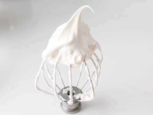 whipped egg white meringue showing a peak on a whisk