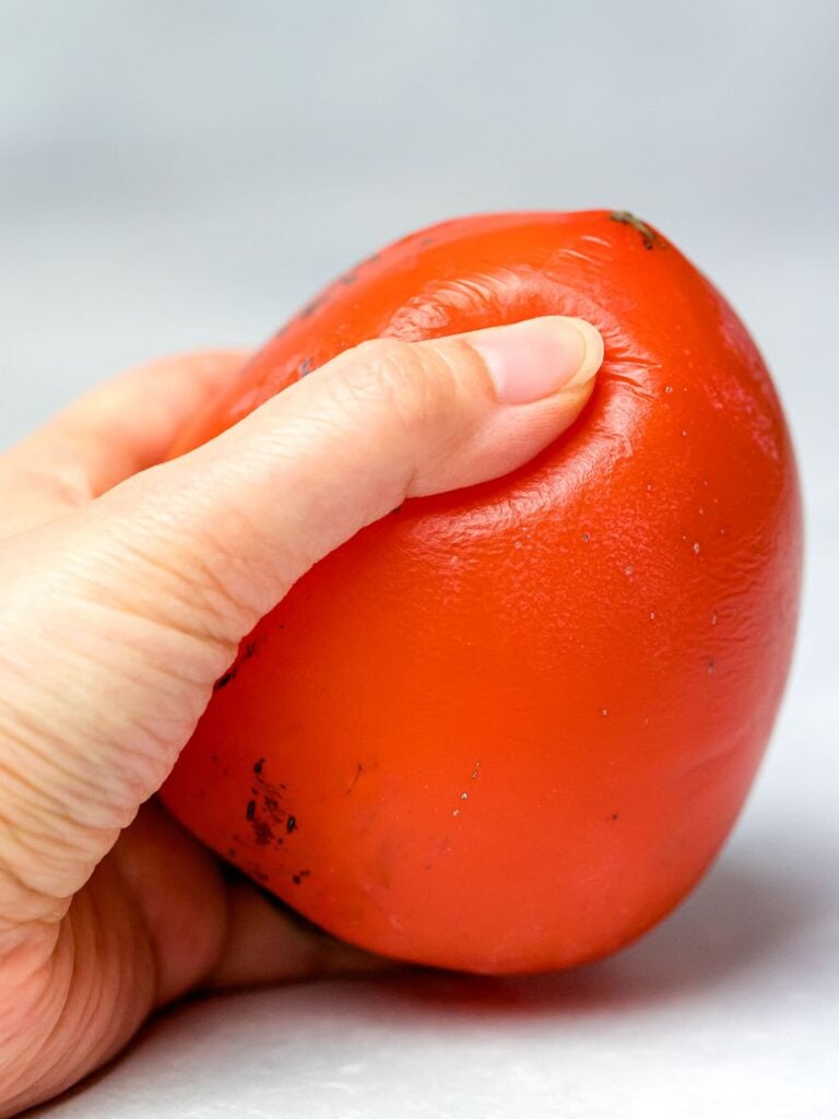 hachiya persimmon being squeezed by a hand to show ripeness