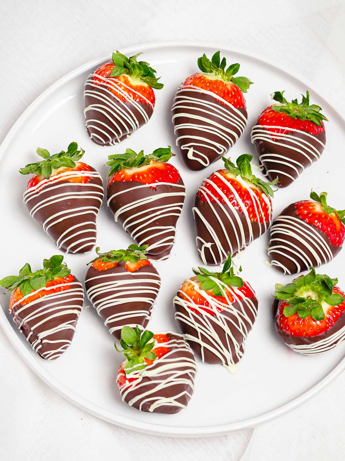 chocolate dipped strawberries with white chocolate decoration on a white plate