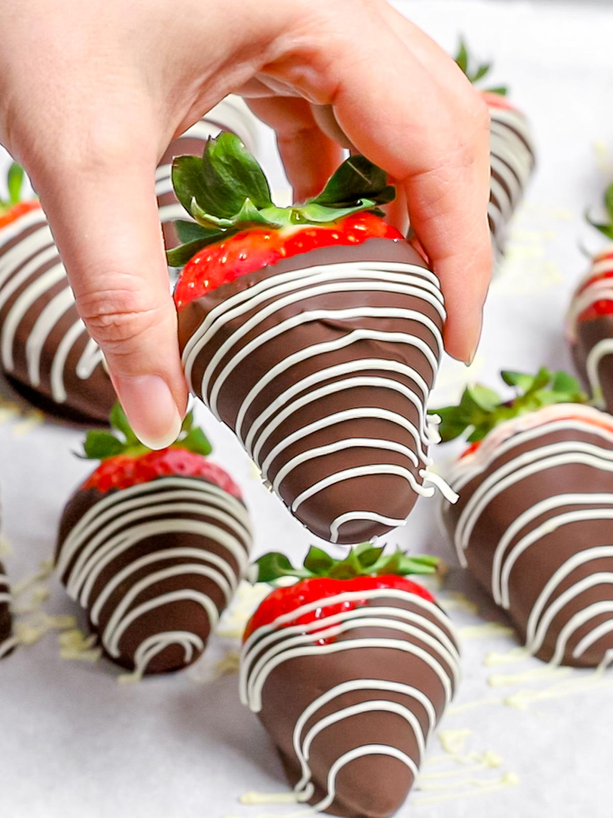 chocolate covered strawberries with white chocolate stripes held by a hand