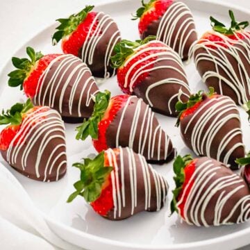 chocolate covered strawberries decorated with white chocolate drizzle on a white plate
