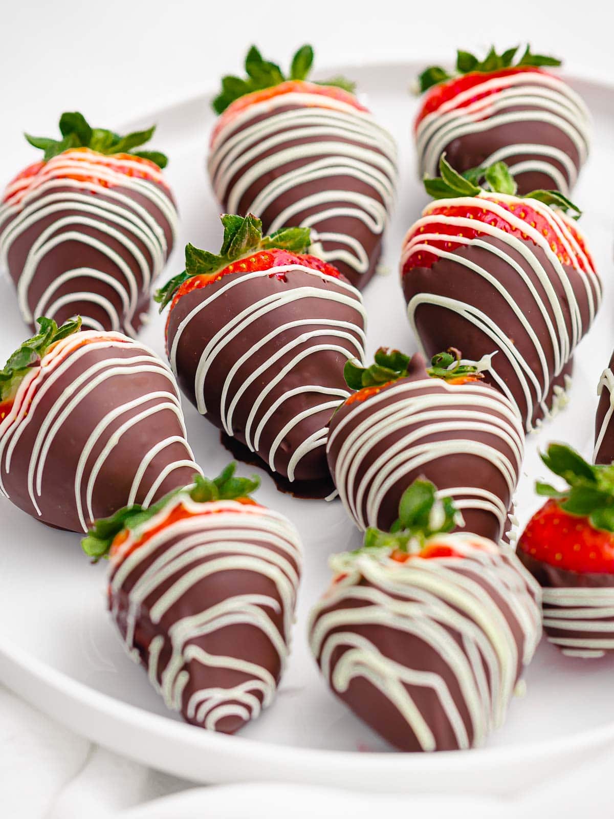 close up of chocolate covered strawberries with white chocolate drizzle on a white plate